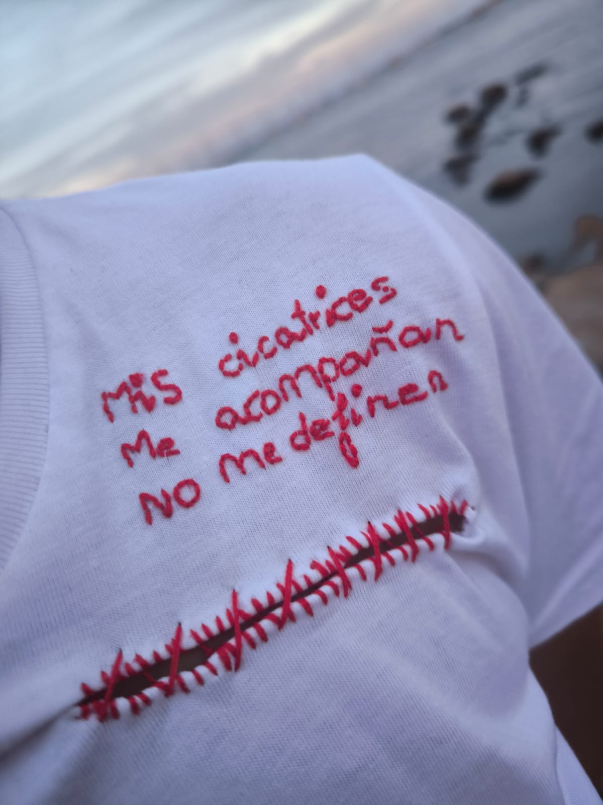 Otra vista de la camiseta La cicatriz, con bordado rojo sobre tejido blanco.