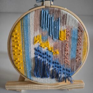 Obra textil abstracta con bordado azul y amarillo sobre tela de reciclaje, en un bastidor