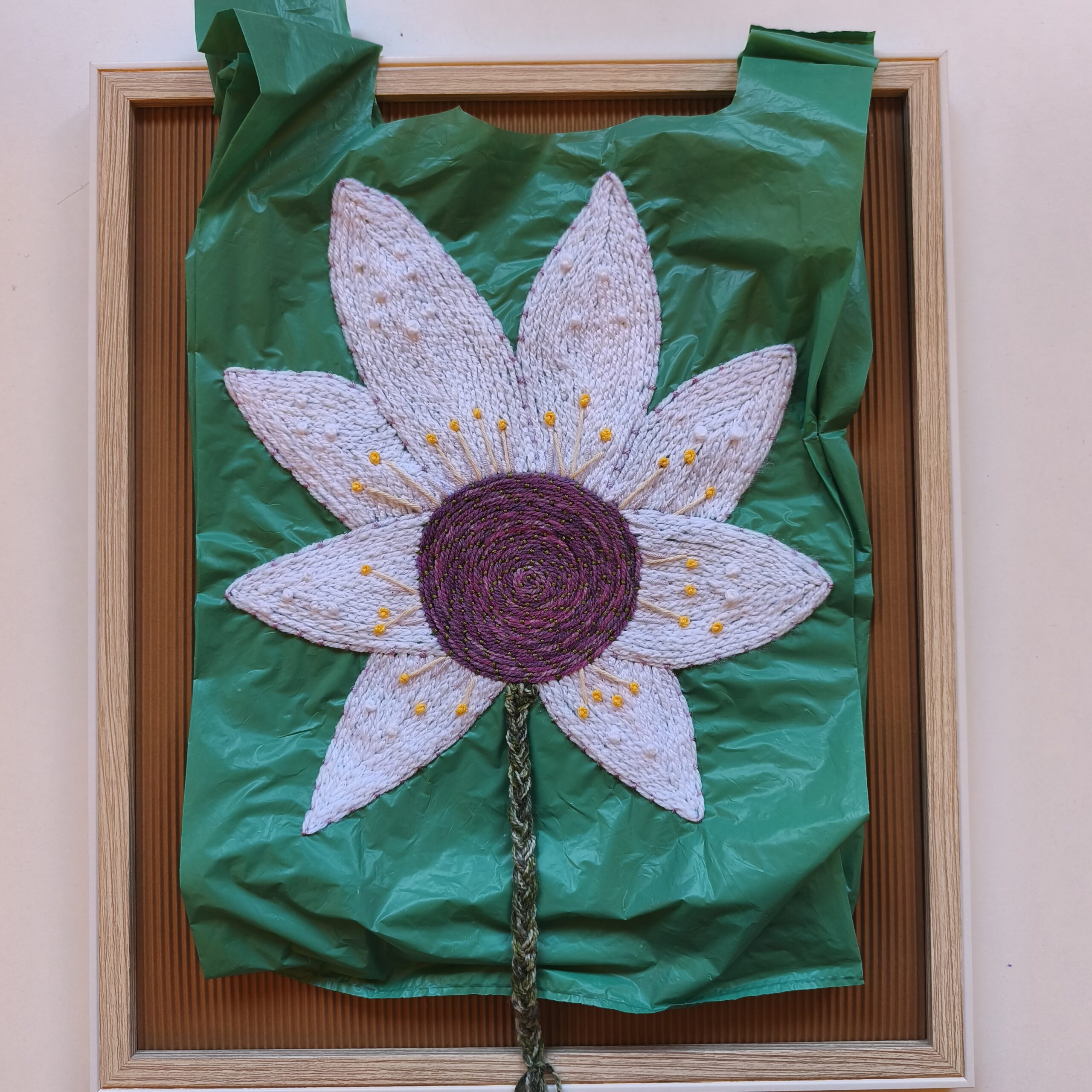 La llegada de la primavera: flor bordada sobre soporte plástico verde, enmarcada en madera